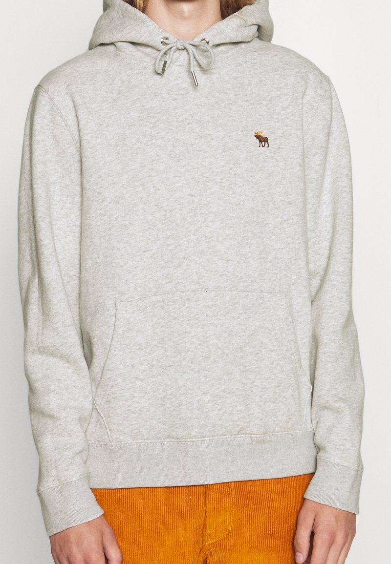 Lichtgrijze hoodie gemaakt van een katoenmix. Trekkoord bij de hals, kangoeroezak en kleine moose borduursel op de borst.