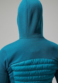 Teal hoodie met een gegroefde textuur op de bovenkant en een gewatteerd paneel op de onderrug. Heeft een getailleerde pasvorm en een zachte stof.