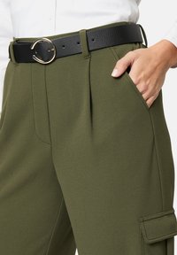 Olivgrüne, hochgeschnittene Hose mit Falten, seitlichen Taschen und einem schwarzen Kunstledergürtel mit einer goldenen runden Schnalle.