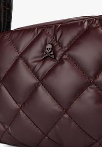 Bolso burdeos acolchado hecho de un material brillante y acolchado; cuenta con un pequeño emblema de calavera negra y un marcado patrón de costura en diamante.
