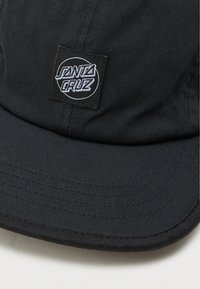 Boné preto feito de tecido texturizado, apresentando um patch circular branco com o texto "SANTA CRUZ" em destaque na frente.