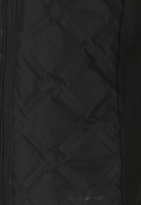 Svart vadderad jacka med texturerat geometriskt mönster, utrustad med hel dragkedja fram och logotypdetalj i botten. Slät tygfinish.