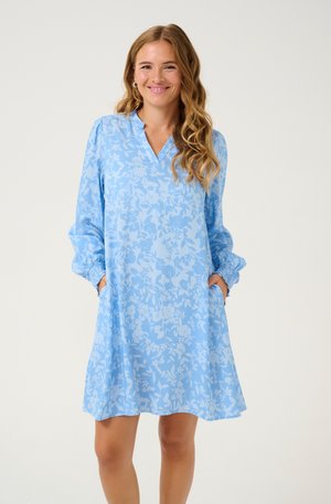 Vestido azul claro con estampado floral, de manga larga y muñecas con puño. Presenta un escote en V y bolsillos laterales. Textura de tela suave.