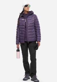 Doudoune violette avec capuche, superposée sur un haut sombre, associée à un pantalon noir. Tient une bouteille d'eau rose, porte des lunettes de soleil teintées et des gants.