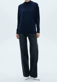 Granatowy sweter z długim rękawem, o wysokim kołnierzu, zestawiony z szerokimi spodniami z ciemnego denimu i szpiczastymi białymi obcasami. Prosty design i gładka tekstura.