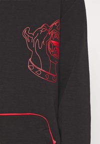 Schwarzer Pullover mit rotem Umriss eines Hundekopfes und einer Halsband. Er hat eine Fronttasche mit kontrastierendem rotem Rand und einer glatten Textur.