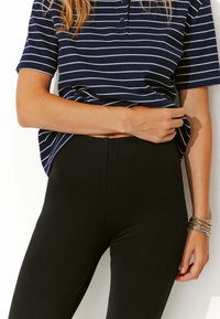 Polo shirt à rayures navy et blanches à manches courtes avec trois boutons, associé à des leggings noirs taille haute et des bracelets superposés sur un poignet.