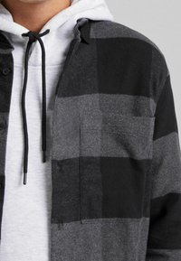 Grå och svart rutigt flanellskjorta med en lapplåda, lager över en ljusgrå huvtröja med svarta dragband.