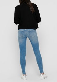 Veste noire courte, jean taille haute bleu clair, coupe slim, délavé, trois poches arrière, associé à des baskets argentées métalliques.