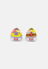 Chaussures Vans colorées présentant un mélange de motifs roses, jaunes et violets, avec des semelles en caoutchouc blanches et un logo rouge sur le talon.