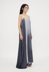 Grijze maxi-jurk met een rechte silhouette en doorschijnende bandjes, met een verlooppatroon van donkergrijs naar lichtgrijs. Soepele stofstructuur.