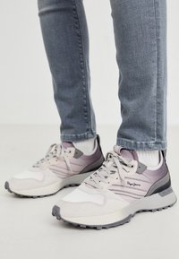 Vita och grå sneakers med texturerat tyg, lila detaljer och en gummisul. Har snören och ränder på sidorna.