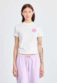 Hvit kortermet t-skjorte med rund hals, som har et rosa grafisk trykk "DICKIES SINCE '22" på venstre bryst. Glatt bomullstekstur.