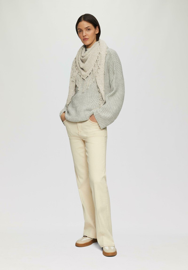 Pull en maille gris clair avec une écharpe beige à franges, pantalon évasé couleur crème et chaussures beiges à fini brillant.