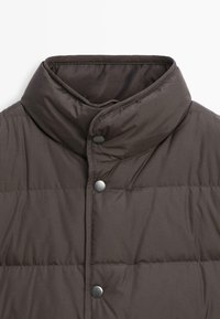 Giacca a vento marrone con colletto alto, caratterizzata da una texture a trapunta, chiusura con bottoni a pressione e una finitura in tessuto liscia.