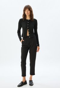 Zwarte geribbelde cardigan met ronde hals en knoopsluiting, gecombineerd met slim zwarte broeken met een geplooid ontwerp en zijzakken.