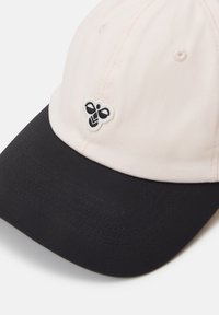 Cap with a light pink cotton body and a black brim. Features a small white and black embroidered logo on the front left panel.