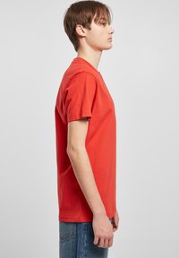 Rotes Baumwoll-T-Shirt mit Rundhalsausschnitt und kurzen Ärmeln, in regular Fit, seitlich an einem Modell gegen einen neutralen Hintergrund präsentiert.