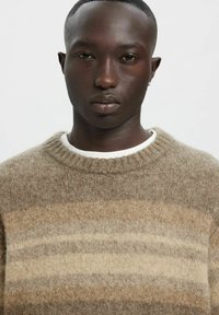 Pull rayé marron avec un col rond côtelé, texture douce, présentant des nuances horizontales de beige et de marron clair.