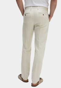 Pantalones de lino beige con un corte relajado, que cuentan con dos bolsillos traseros y detalles de costura sutiles. Combinados con zapatos marrones de tipo slip-on.
