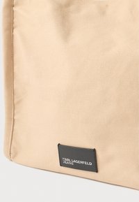 Bézs színű vászontáska fekete címkével, rajta a "KARL LAGERFELD JEANS" felirat. Simább textúrájú, masszív kivitelű, mindennapi használatra alkalmas.