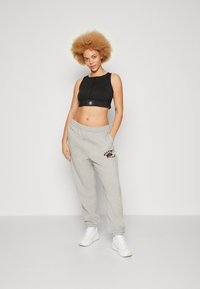 Czarny crop top z wysokim kołnierzem i centralnym szwem, w połączeniu z szarymi spodniami dresowymi z logo. Model nosi białe buty sportowe.