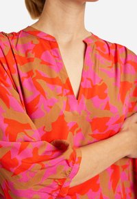 Kleurrijke blouse met een V-hals en driekwart mouwen. Gemaakt van lichtgewicht stof met een gedurfd roze en oranje abstract patroon.