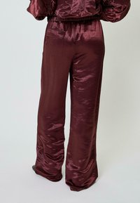 Bordo atlaso plataus pjūvio kelnės su lygiu, blizgučiu paviršiumi, turinčios užpakalinį kišenę ir elastinę juostą.