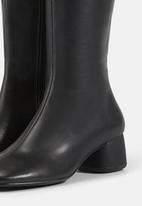 Bottines en cuir noir avec une texture lisse, fermeture éclair et un talon carré modeste. Présente une silhouette ajustée et un bout arrondi.
