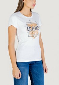 Camiseta blanca de manga corta con diseño gráfico floral y texto "LIU JO" en azul marino. Confeccionada en tela de algodón, corte ajustado y textura suave.