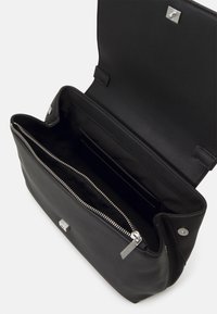Black leather handbag with flap open, showing zippered inner compartment and slip pocket inside. Silver hardware and Calvin Klein branding.