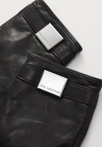 Black leather gloves with a smooth texture. Features silver-tone square labels embossed with "KARL LAGERFELD" and multiple stitching details.