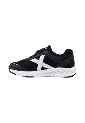 Zapatilla deportiva en blanco y negro con parte superior de malla, diseño "X" blanco en el lateral, cordones negros y suela blanca gruesa con dibujo texturizado.