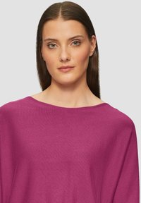 Fuchsia oversized gebreide top met een brede halslijn en een textuurafwerking. Glad materiaal valt voorzichtig over de schouders.
