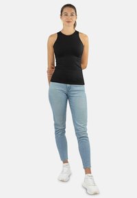 Schwarzes ärmelloses Oberteil in figurbetonter Passform, aus leichtem Stoff. Kombiniert mit hellblauen Skinny-Jeans und weißen Sneakers.