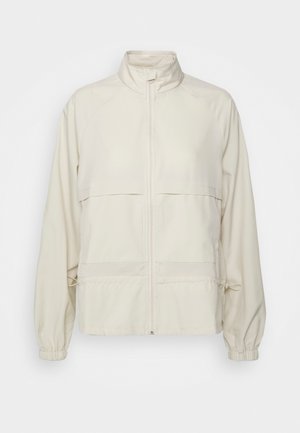 Vaalean beige vetoketjullinen takki, joka on valmistettu sileästä kankaasta. Varustettu ylösnostettavalla kauluksella, kahdella rintataskulla, elastisilla hihoilla ja säädettävällä nyörillä vyötäröllä.