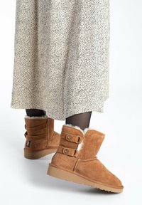 Stivaletti ankle in suede marrone con fodera in shearling, dotati di due bottoni laterali e suola in gomma testurizzata. Abbinati a un vestito a pois.