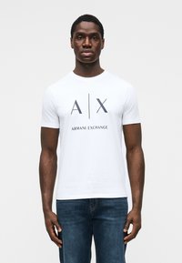 Tricou alb cu mâneci scurte, cu logo negru imprimat "A|X" și textul "ARMANI EXCHANGE" dedesubt, realizat din țesătură de bumbac netedă.