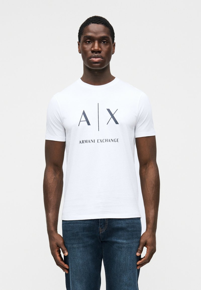 Tricou alb cu mâneci scurte, cu logo negru imprimat "A|X" și textul "ARMANI EXCHANGE" dedesubt, realizat din țesătură de bumbac netedă.