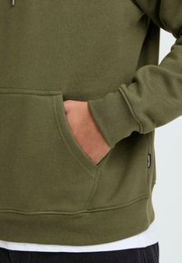 Olive green sweatshirt with a front pocket, ribbed cuffs, and hem. Features a subtle texture, stitched seams, and a small brand label on the side.