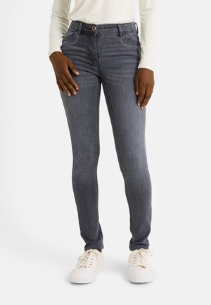Jeans ajustados de color gris oscuro con bolsillos delanteros, cierre de botón y detalles de costura blanca, combinados con zapatillas blancas.