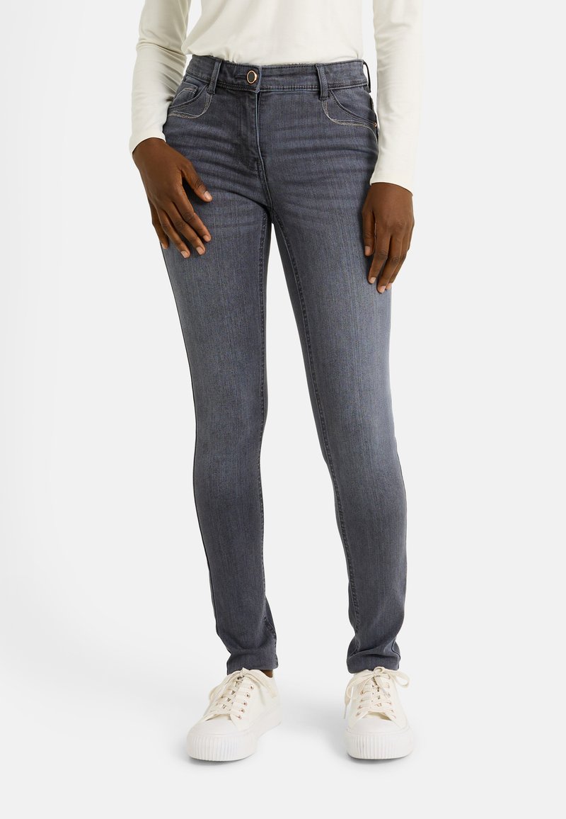Jeans ajustados de color gris oscuro con bolsillos delanteros, cierre de botón y detalles de costura blanca, combinados con zapatillas blancas.