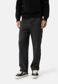 Šedé kalhoty na míru vyrobené z měkké tkaniny, s rovnými nohavicemi. Nosí se s černým svetr a tmavými teniskami.