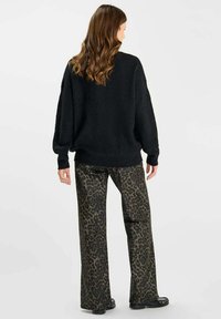 Maglione oversize nero in tessuto texturizzato abbinato a pantaloni larghi leopardati verde scuro, con una vestibilità morbida e un leggero luccichio.