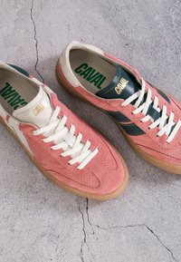Paire de baskets en daim rose avec lacets blancs, accents verts et blancs, et semelles en gomme sur une surface en béton gris fissurée.