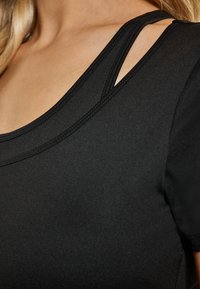 Top negru ajustat, cu o textură fină, decolteu rotund și curele încrucișate în zona umerilor pentru un plus de detaliu.