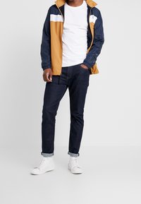 Leichte, blockfarbige Jacke in Braun, Marineblau und Weiß; kombiniert mit einem weißen T-Shirt, dunklen Jeans und weißen Sneakers.