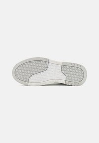Suola di scarpa in materiale gommoso texturizzato, caratterizzata da un motivo geometrico e un design semplice. Predominantemente bianca con accenti grigi.