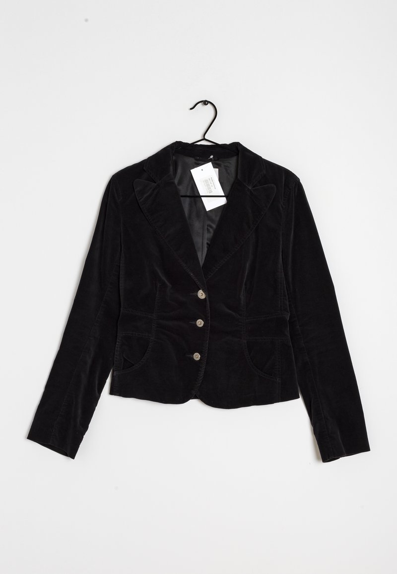 Blazer en velours noir à trois boutons, col à revers et poches avant, suspendu à un cintre noir sur un fond blanc.