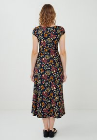 Das blumige Maxikleid in Marineblau hat kurze Ärmel, ein eng anliegendes Oberteil und einen fließenden Rock. Der Stoff zeigt bunte Blumen und Blätter.